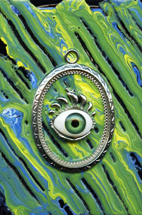 A silver eye pendant on green poured paint
